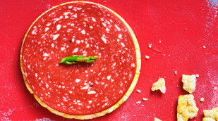 high-angle-view-of-a-slice-of-veggie-salami-on-a-rice-cake,-on-a-red-textured-surface-10x6