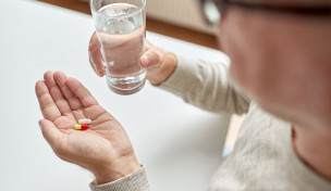 Männerhände halten Tabletten und Wasserglas