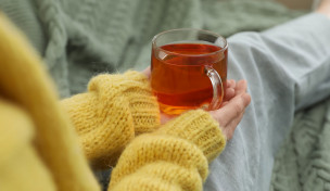 Frau mit gelben, flauschigen Pullover sitzt und hält eine Tasse Tee in beiden Händen