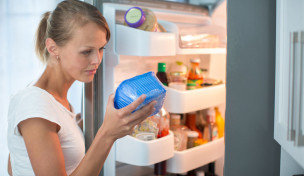 Frau vor geöffnetem Kühlschrank sieht sich eine Lebensmittelverpackung an