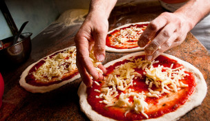 Pizzabäcker belegt Pizza mit Käse