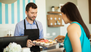 Mann zeigt einer Frau Cupcakes an einer Kuchentheke Mann zeigt einer Frau Cupcakes an einer Kuchentheke