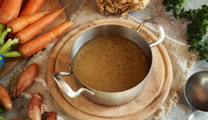 knochenbruehe in einem topf auf einem tisch mit gemüse im hintergrund