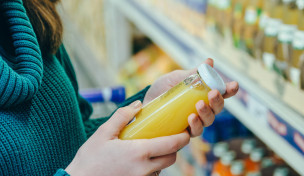 Frau liest Beschriftung einer Saftflasche vor einem Supermarktregal