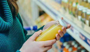 Frau liest Beschriftung einer Saftflasche vor einem Supermarktregal