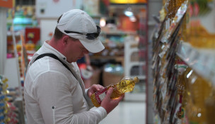Mann im Supermarkt liest Etikett einer Ölflasche