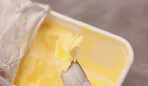 Margarine auf Messerspitze. Im Hintergrund ist eine geöffnete Maraginepackung.