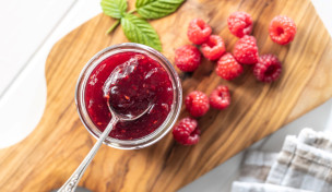 Himbeermarmelade im Glas neben frischen Himbeeren