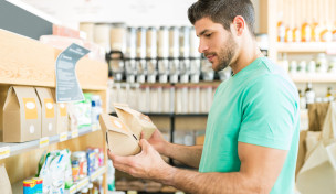 Ein Mann vergleicht im Supermarkt zwei Verpackungen