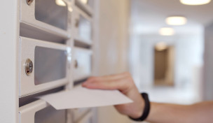 Eine Hand schiebt einen Brief in den Briefkasten