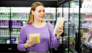 Frau schaut sich zwei Käseverpackungen im Supermarkt an
