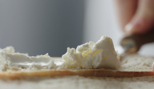 eine Brotscheibe wird mit Frischkäse bestrichen