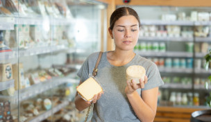 Frau in der Käseabteilung schaut sich zwei Käseverpackungen an