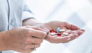 Person hält verschiedene Kapseln und Tabletten in der Hand