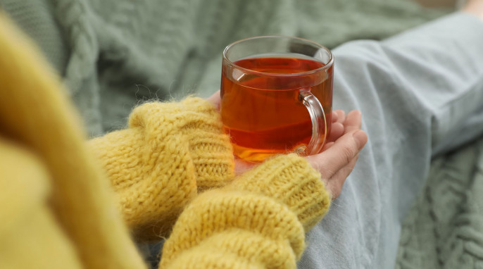 Frau mit gelben, flauschigen Pullover sitzt und hält eine Tasse Tee in beiden Händen