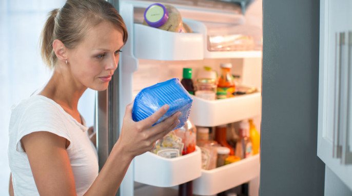 Frau vor geöffnetem Kühlschrank sieht sich eine Lebensmittelverpackung an