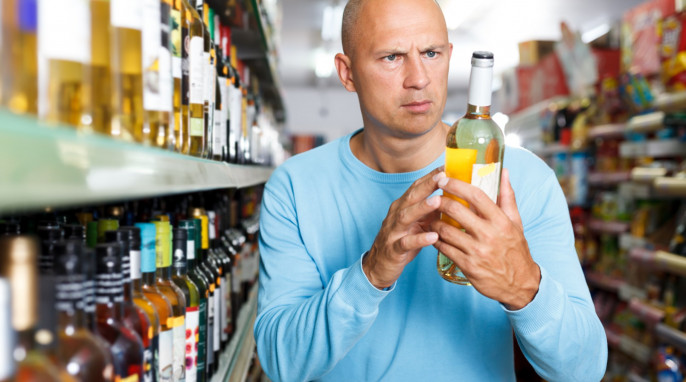 Mann betrachtet Flasche im Supermarkt - mit oder ohne Alkohol?