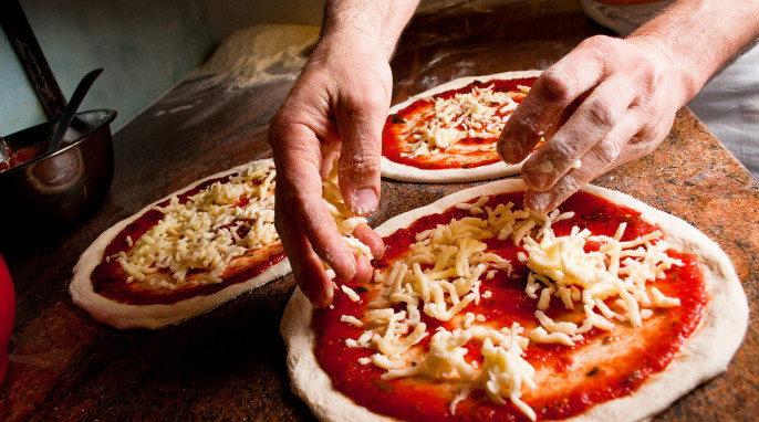 Pizzabäcker belegt Pizza mit Käse