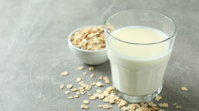 Glas mit Hafermilch, daneben kleine Schüssel mit Haferflocken