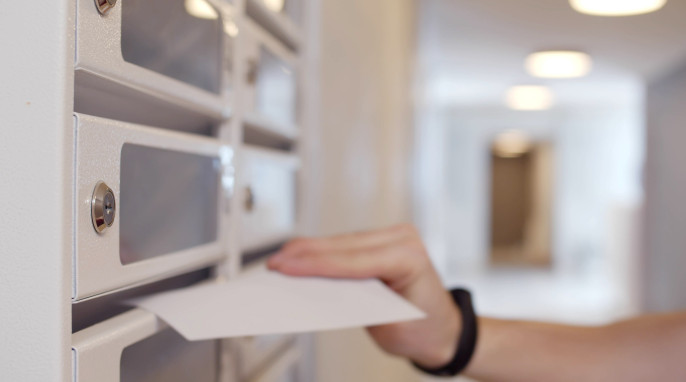Eine Hand schiebt einen Brief in den Briefkasten