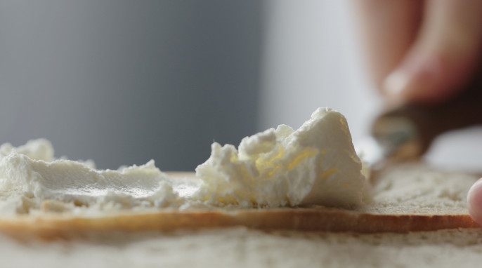 eine Brotscheibe wird mit Frischkäse bestrichen