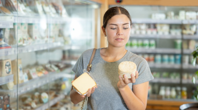 Frau in der Käseabteilung schaut sich zwei Käseverpackungen an