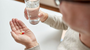 Männerhände halten Tabletten und Wasserglas