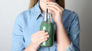 Frau trinkt mit Strohhalm grünes Shake aus einer Flasche
