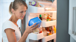 Frau vor geöffnetem Kühlschrank sieht sich eine Lebensmittelverpackung an