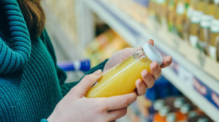 Frau liest Beschriftung einer Saftflasche vor einem Supermarktregal