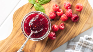 Himbeermarmelade im Glas neben frischen Himbeeren