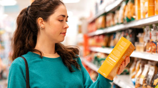 Junge Frau liest Zutatenverzeichnis vor einem Regal im Supermarkt