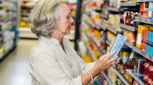 Frau liest Beschriftung einer Schachtel im Supermarkt