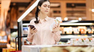 Frau mit Smartphone begutachtet kritisch eine Packung