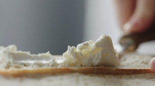 eine Brotscheibe wird mit Frischkäse bestrichen