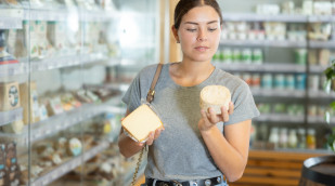 Frau in der Käseabteilung schaut sich zwei Käseverpackungen an